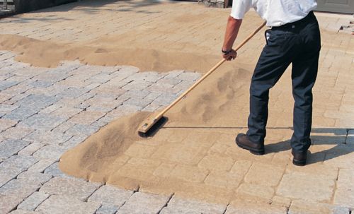 A man spreading polymer sand over pavers