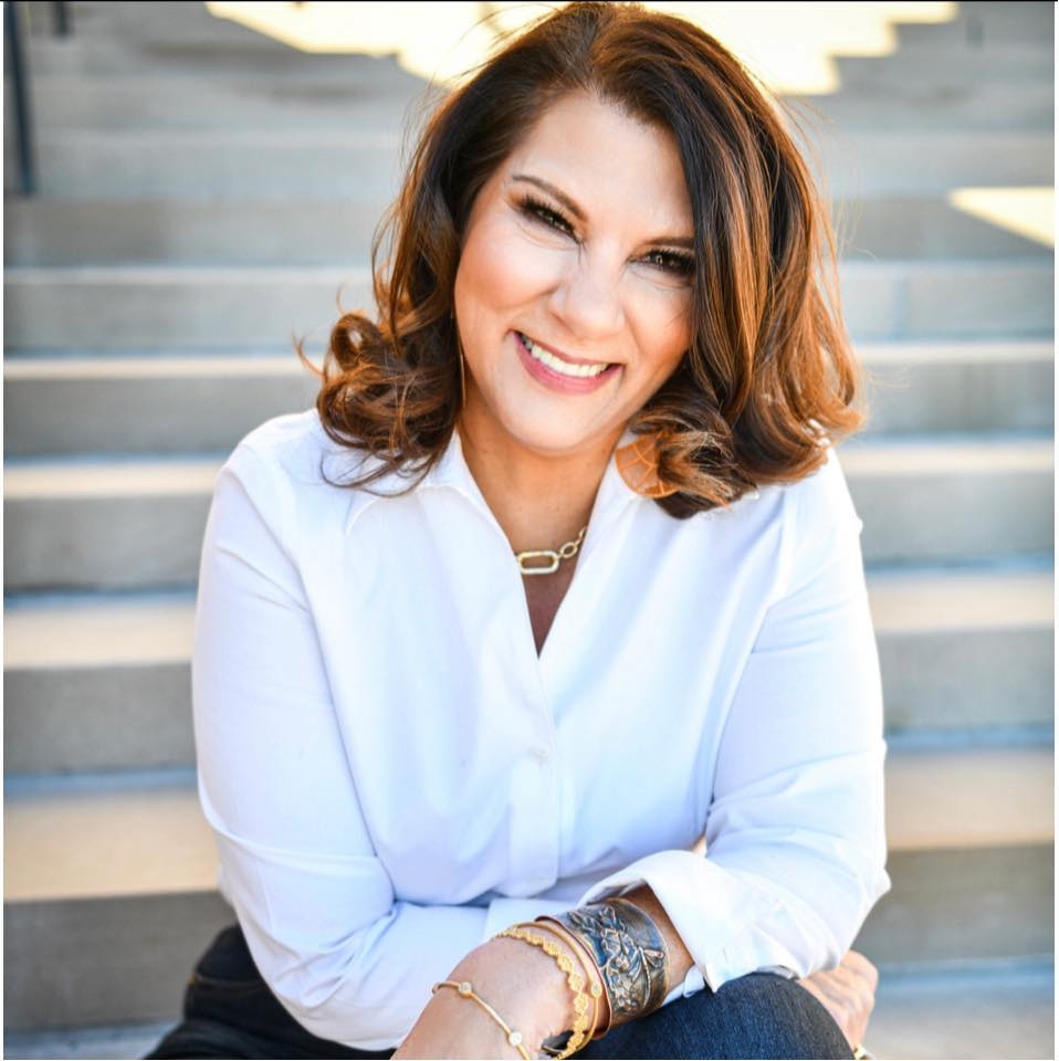 A white woman with reddish hair wearing a white shirt and jewelry