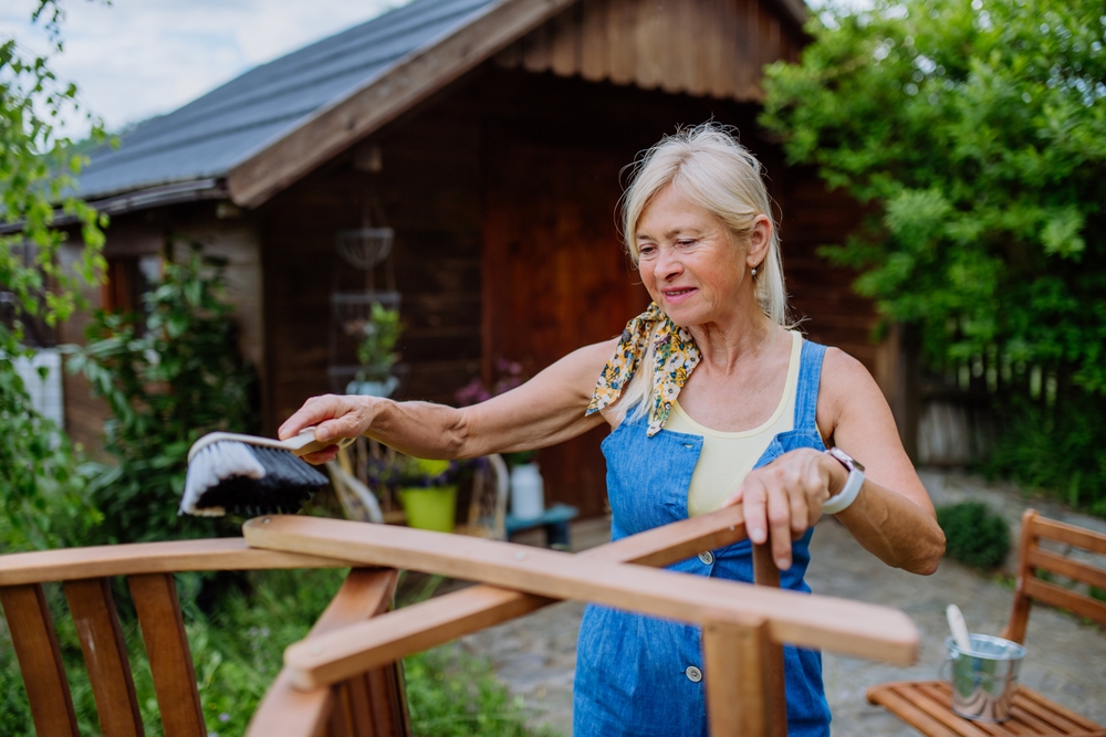 A white, blong haired woman brushing the bottom of a n outdoor chair