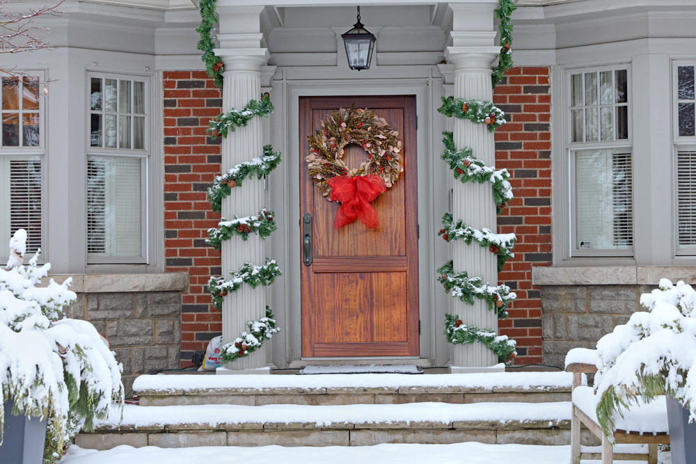 A white house with columns wrapped in green garlands and a Christmas wreath on the door.