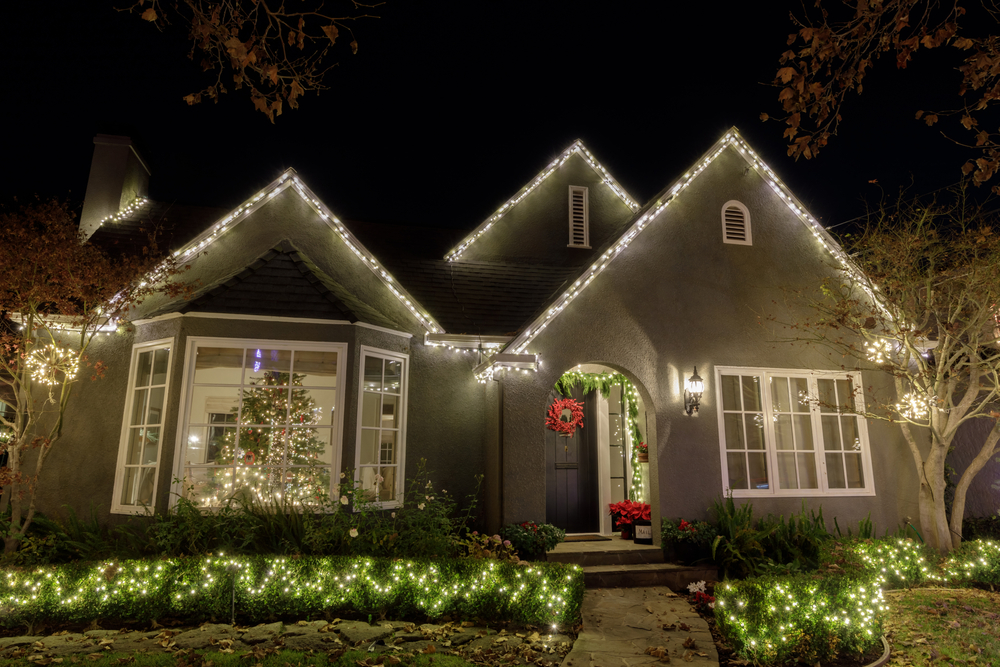 A house with Christmas lights on the roof and hedge.