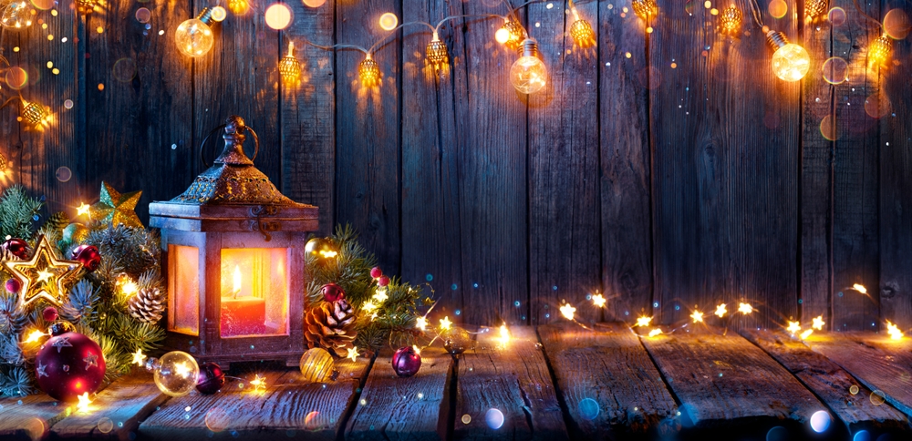 A lantern and fairy lights with garlands sitting on a plank table.