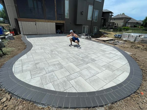 A man crouched on a paving stone driveway