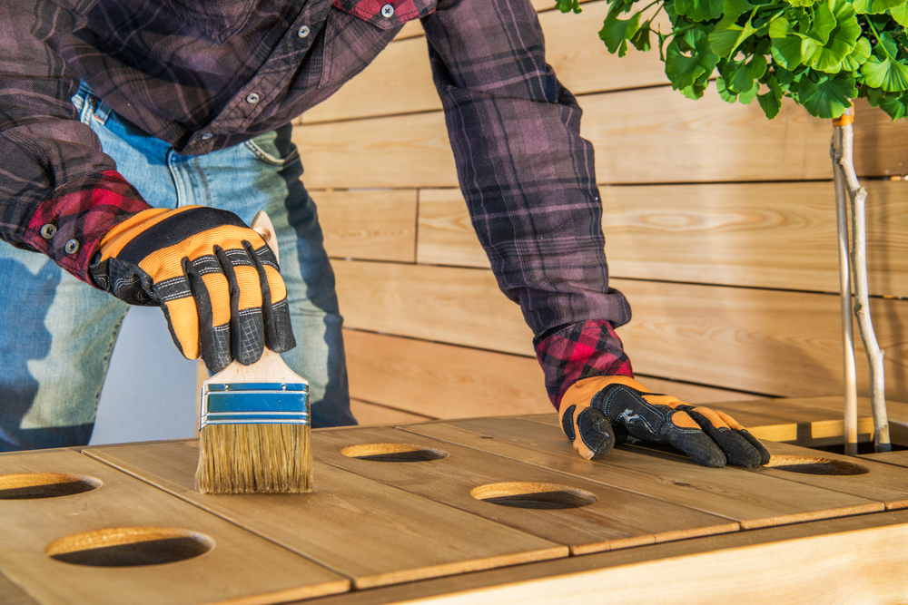 A man brushing sealant onto a wooden piece of furniture