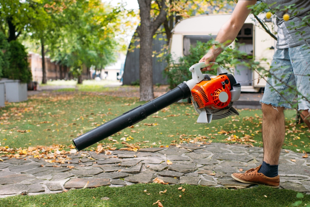 A man blowing leaves of a path of paving stones.