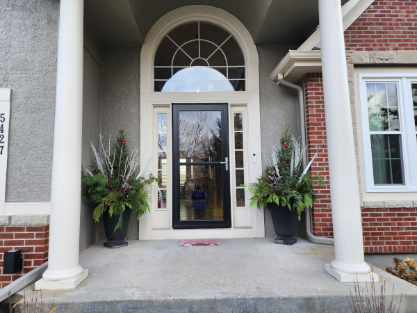 A porch with two columns and two planters flanking a door.