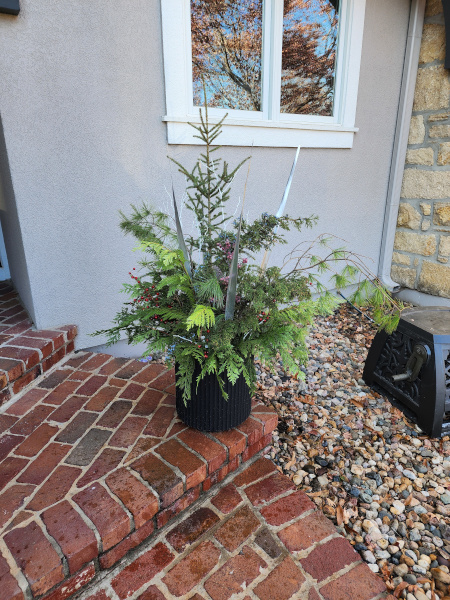 A fall themed planter with evergreen plants on a brick porch.