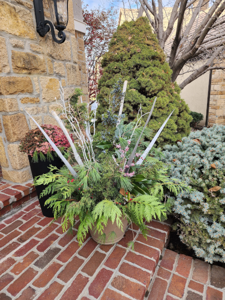 A planter on a porch in front of other planters and evergreens.