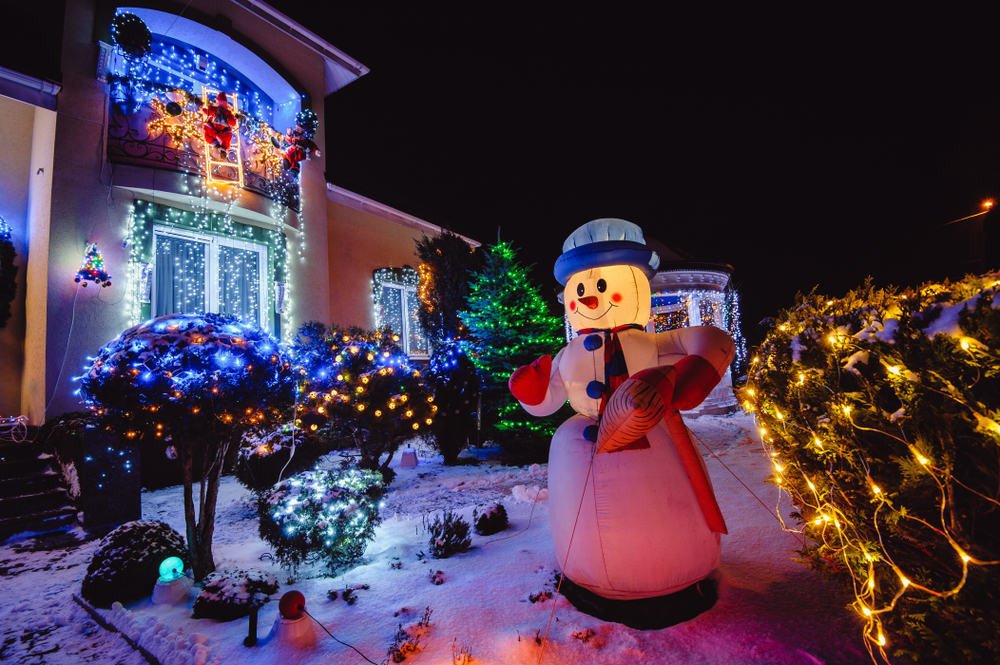 An inflatible snowman by lighted shrubs and a docorated house.